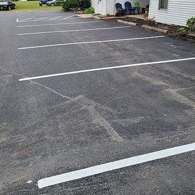 A parking lot with white lines painted on it undergoes seal coating.
