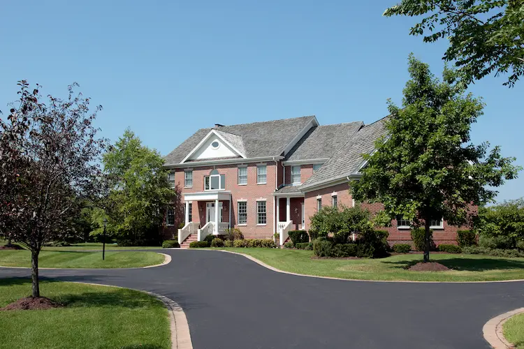 An asphalt driveway leading to a large brick home.