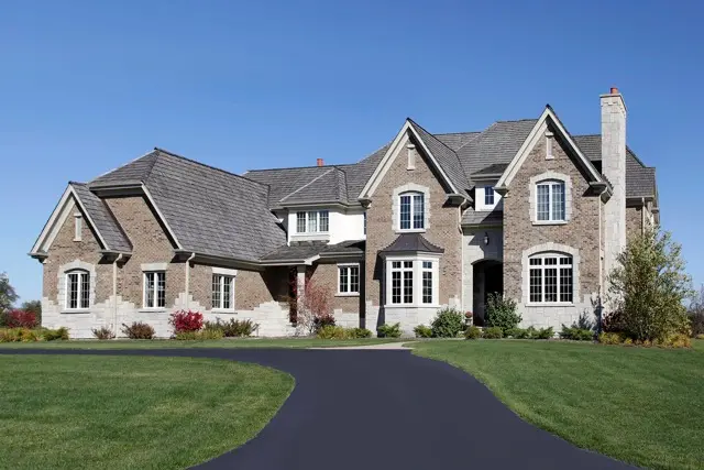 A large house with a freshly sealed asphalt driveway leading to it.