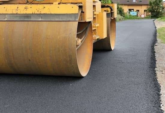 An asphalt paving machine rolling a driveway, smoothing out freshly laid asphalt.