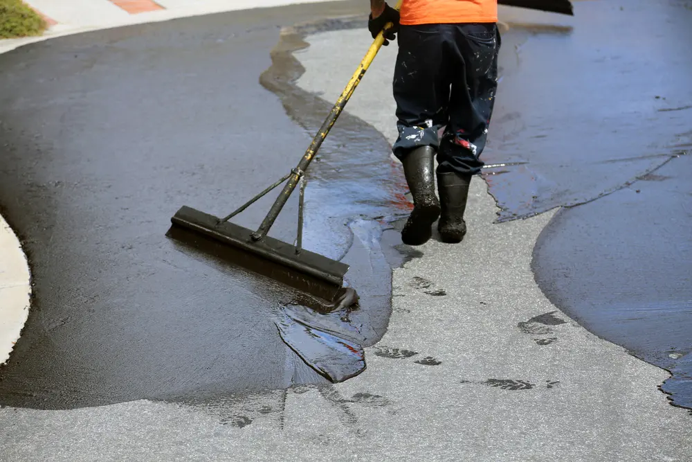 A man performing preventive asphalt paving maintenance by cleaning a paved road with a broom.