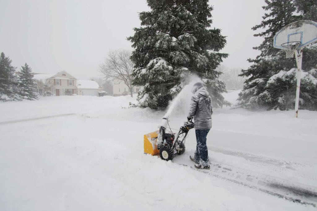 A person snowplowing an asphalt driveway during winter blizzard.