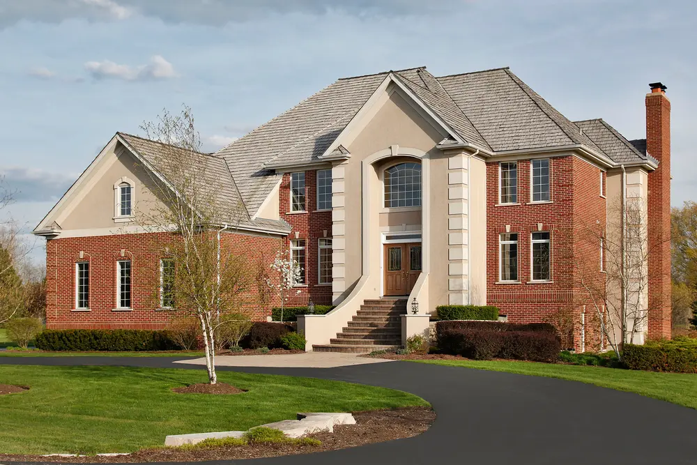 A large brick home with a driveway leading to it that requires regular maintenance for the asphalt surface.