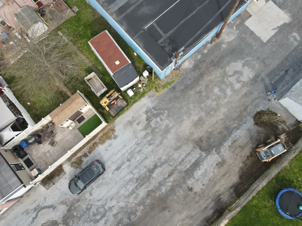 Before photo of a parking lot from Nathan Paving, featuring uneven asphalt surfaces and visible wear, indicating the need for repair and maintenance. Overgrown grass is present along the edges.