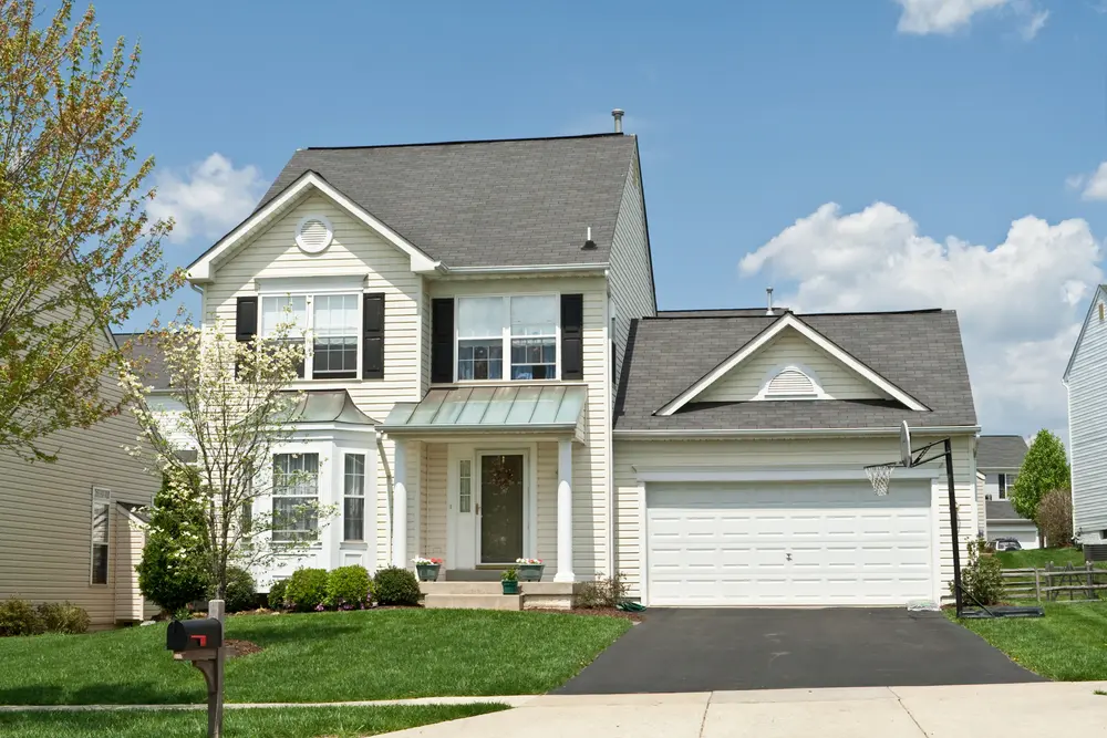 A home with a garage and an asphalt driveway.|A large brick home with a driveway leading to it.