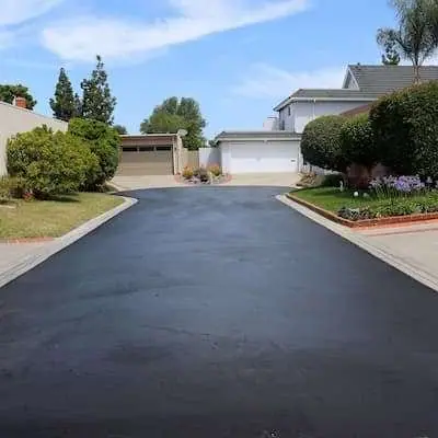 An asphalt driveway being seal-coated, with half the driveway showing a new black surface.