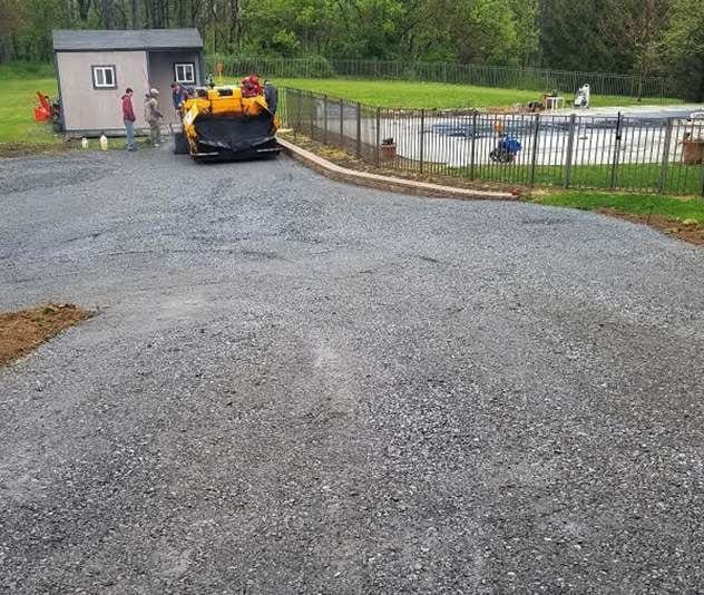 A work site showing the preparation of a foundation before asphalt paving, with gravel laid out.