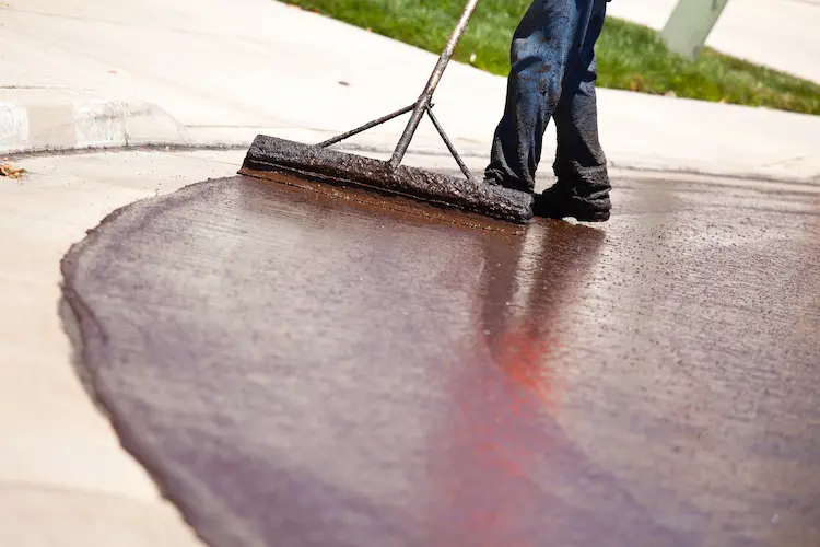 A man is using a broom to seal coating a driveway