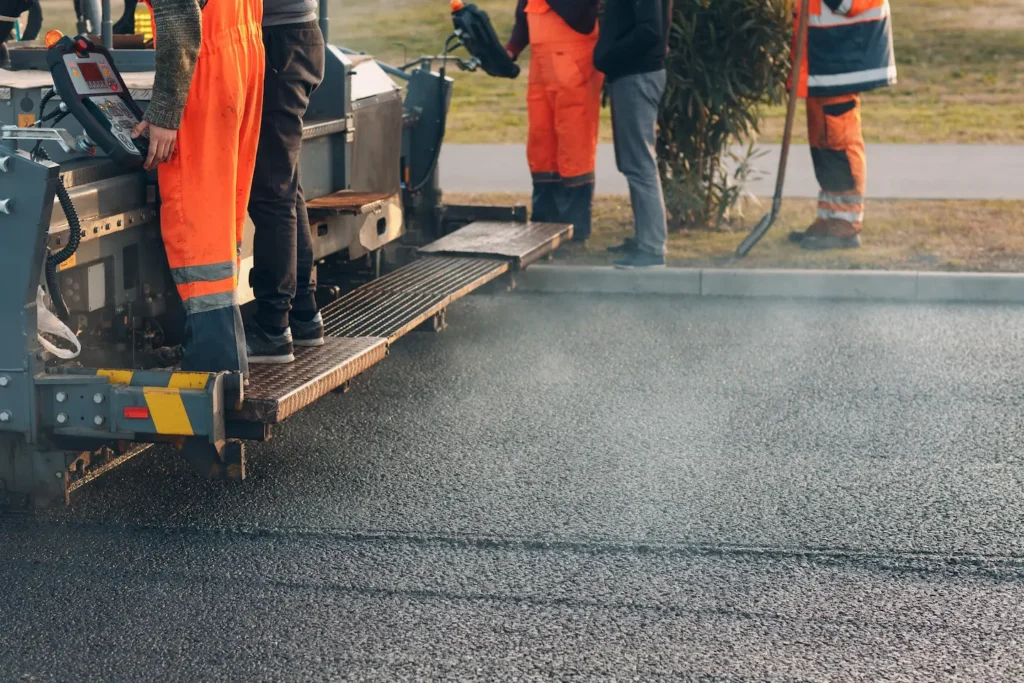 A group of workers from the local paving company are paving a road.