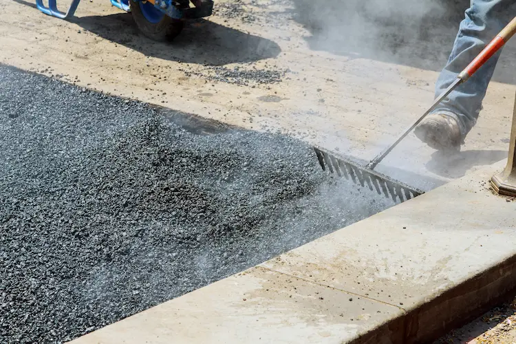 A man is maintaining an asphalt sidewalk with a rake.