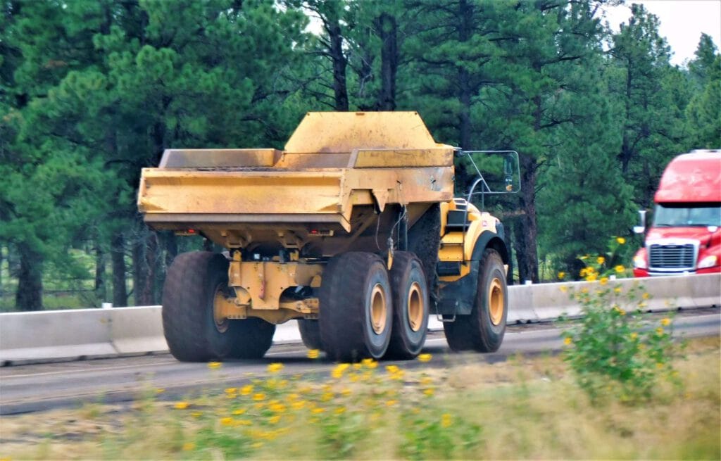 A bright yellow dumper truck is parked on a construction site, surrounded by dirt and gravel. The truck features a large bed for transporting materials and has a sturdy design typical of heavy machinery.