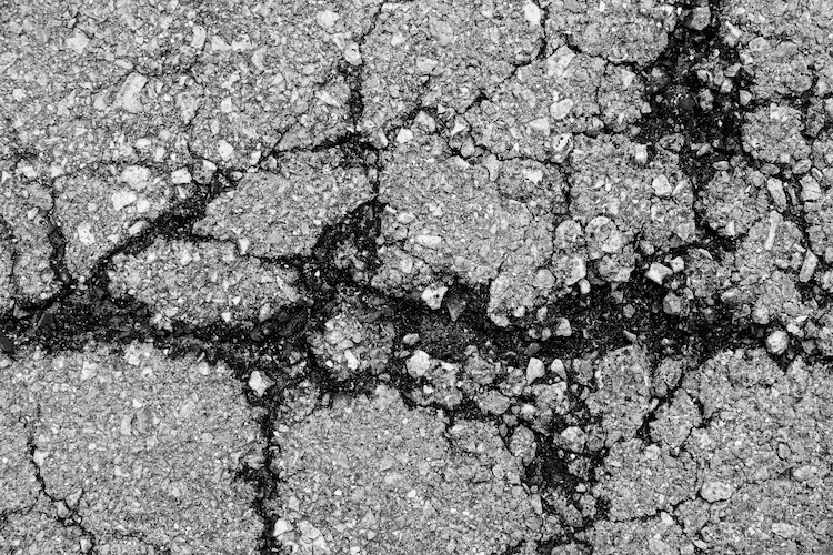 A black and white photo showcasing a cracked road needing asphalt crack repair.