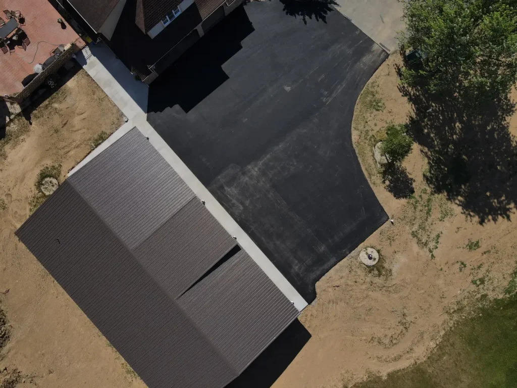 A completed driveway extension in Carlisle, featuring a smooth, dark asphalt surface, bordered by neat grass edges. The scene is well-lit and showcases the driveway's new, extended area.