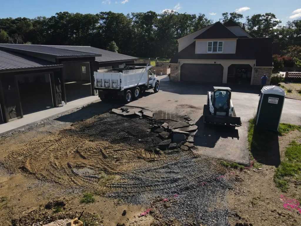 A before image of a residential driveway extension in Carlisle shows a gravel surface with dirt patches, surrounded by grass. The area is uneven and lacks a defined edge, indicating a need for improvement.