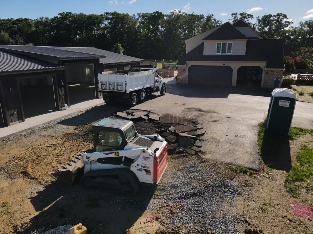 Before photo of a residential driveway extension in Carlisle, showcasing a narrow, uneven gravel path leading to a small area of grass, surrounded by a brick border and a wooden fence in the background.