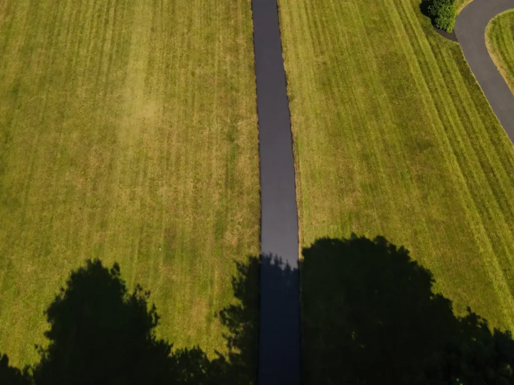 A newly sealed asphalt driveway in Carlisle, showcasing a smooth, glossy black surface with clean edges. The driveway is bordered by green grass and features a slight incline.