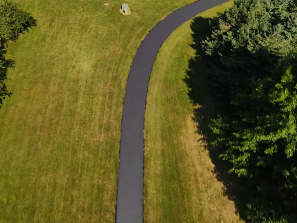 Alt text: A freshly sealed black asphalt driveway in Carlisle, showing a smooth, glossy surface with clear edges, surrounded by green grass and a few scattered leaves, reflecting a well-maintained property.