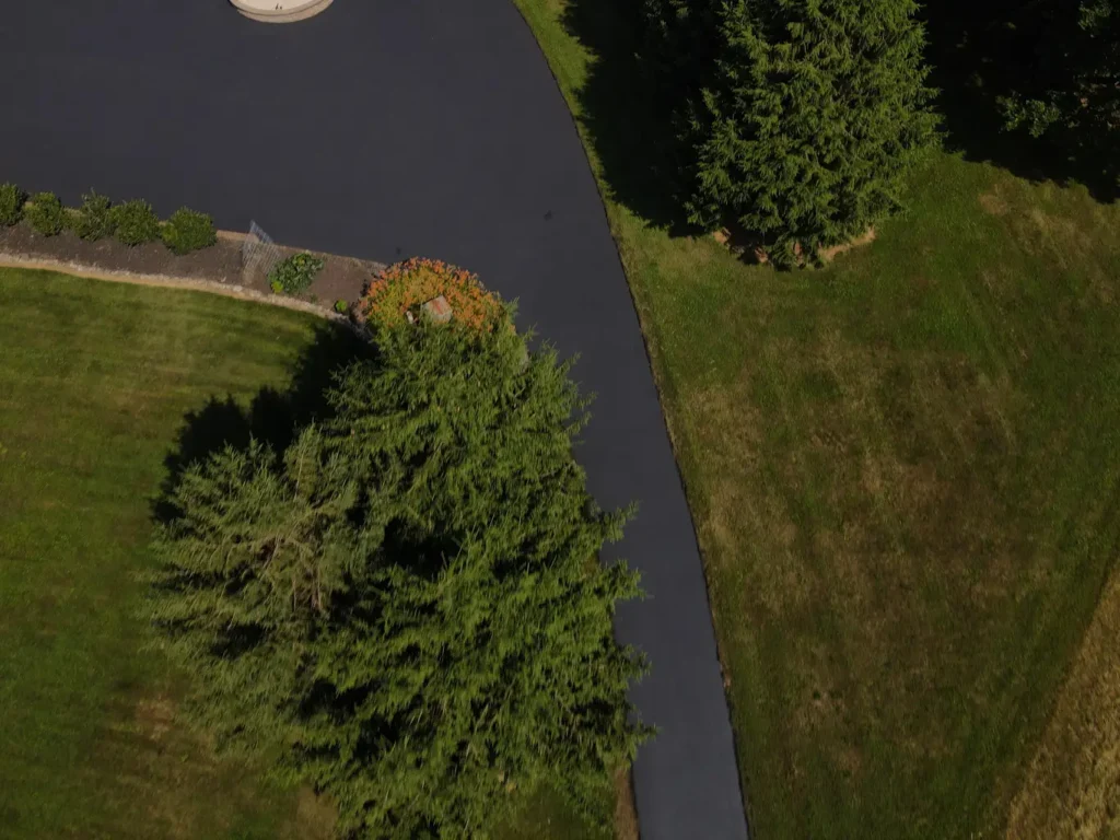 Freshly sealed black asphalt driveway in Carlisle, featuring a smooth, shiny surface. Edges are well-defined, and surrounding area shows a neat, tidy appearance with greenery in the background.