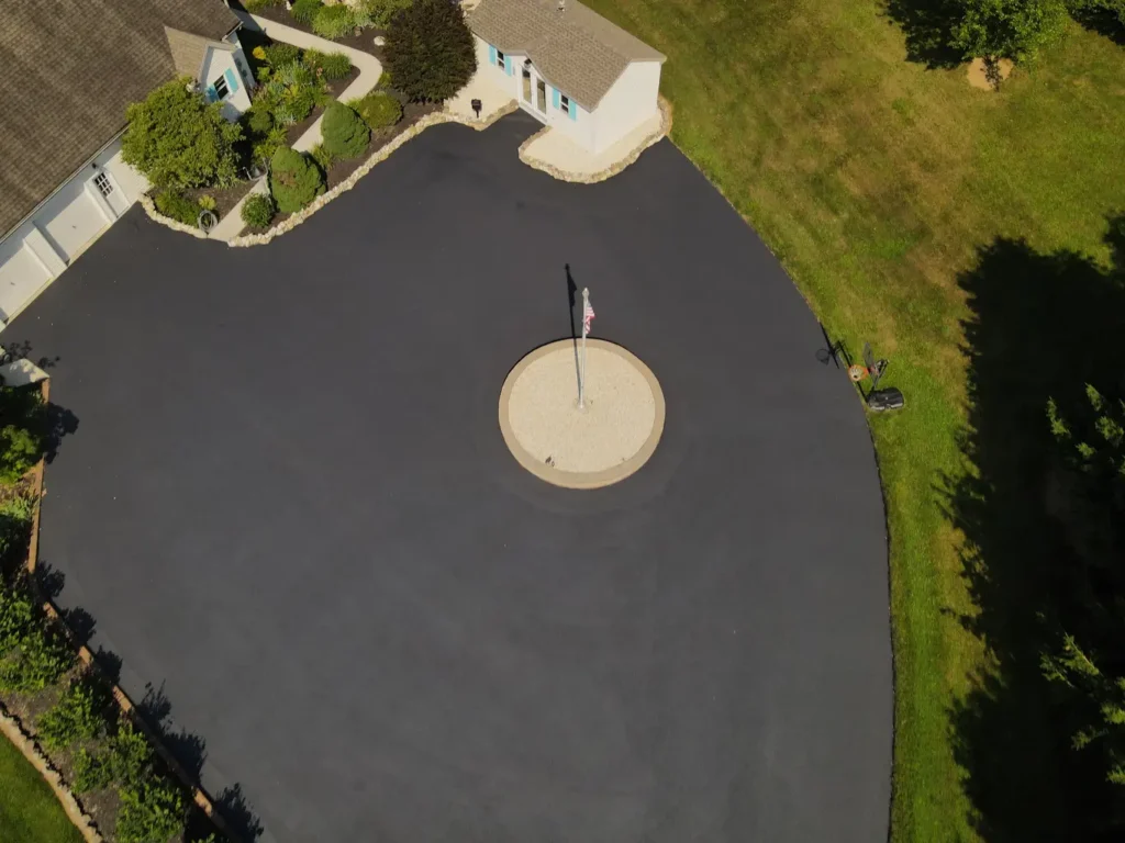 A freshly sealed black asphalt driveway in Carlisle, showing a smooth, glossy surface and clean edges. Surrounding grass is green, and the sky is clear, highlighting the driveway's rejuvenated appearance.