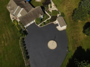 Alt text: A freshly sealed black asphalt driveway in Carlisle, featuring a smooth, shiny surface with a clear distinction from the surrounding grass and concrete. The image is bright and well-lit.