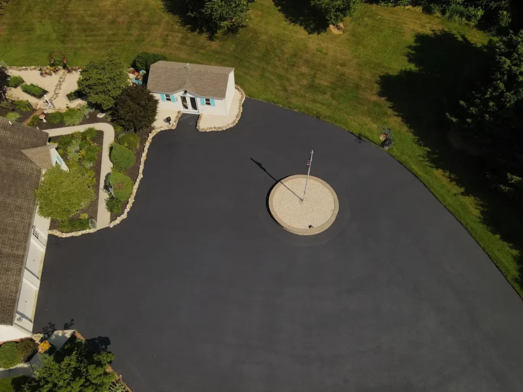 Freshly sealed black asphalt driveway with a smooth, shiny surface, bordered by green grass on one side. The image captures a revitalized appearance, showcasing the effective sealing process.