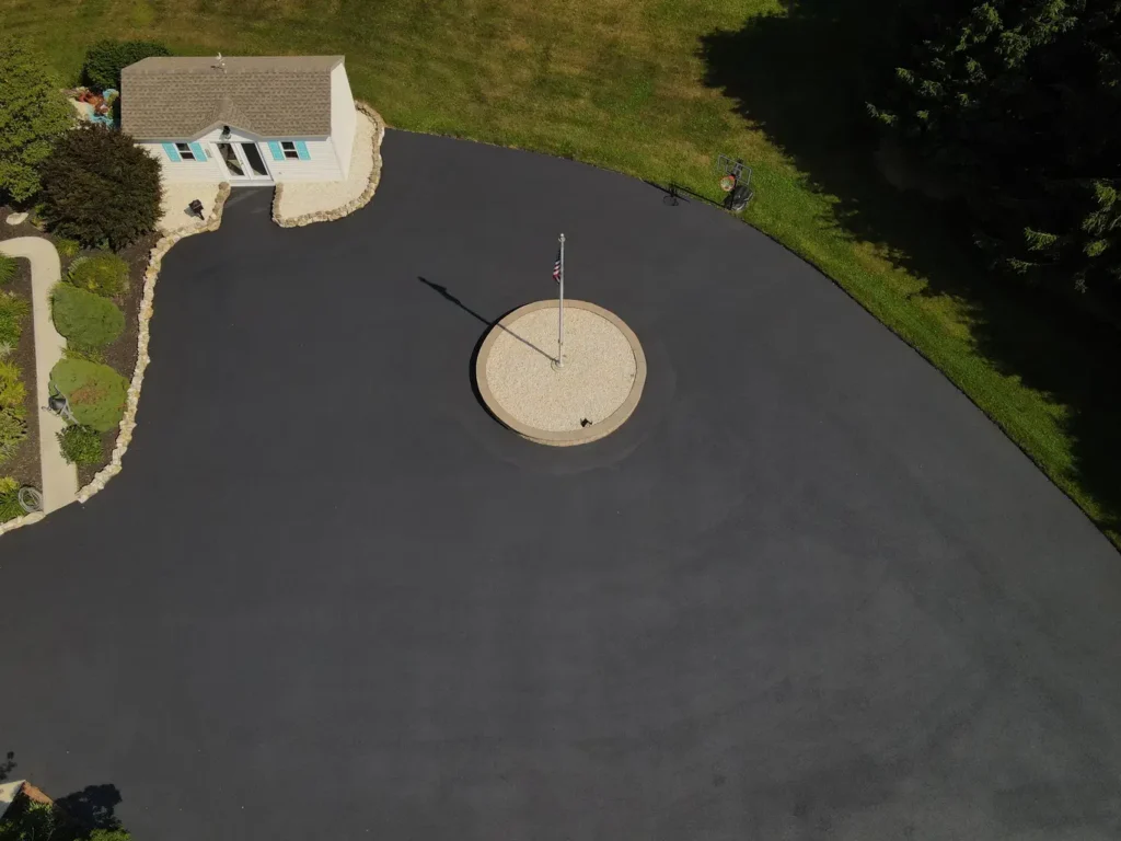 A newly sealed asphalt driveway in Carlisle, showcasing a smooth, glossy surface. The driveway is surrounded by green grass and white gravel, highlighting the clean edges and fresh appearance.