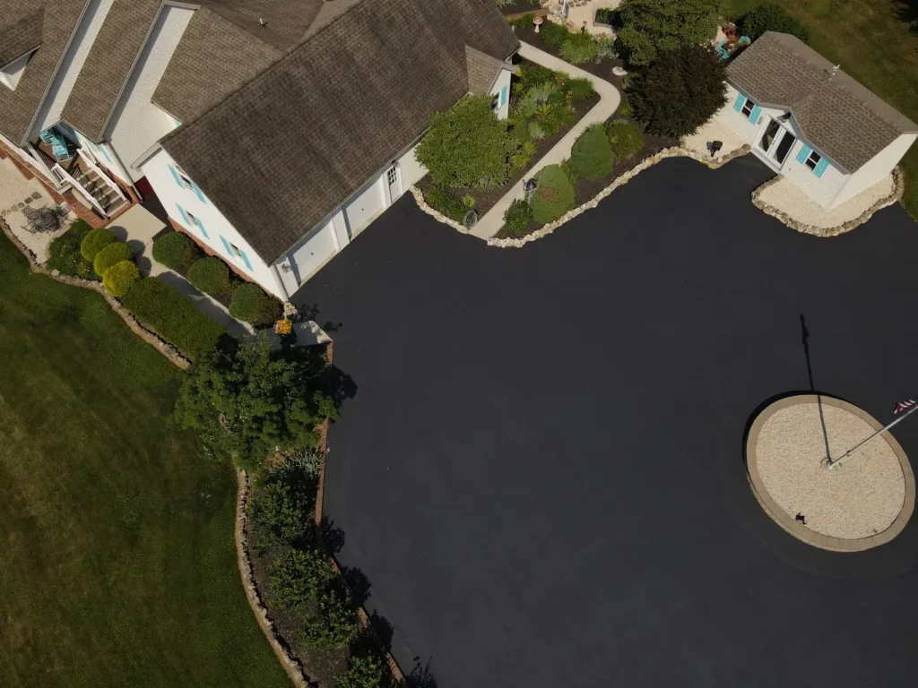 A freshly sealed black asphalt driveway in Carlisle, showing a smooth, shiny surface with a clear blue sky above and green grass bordering the edges. Ideal condition for residential paving.