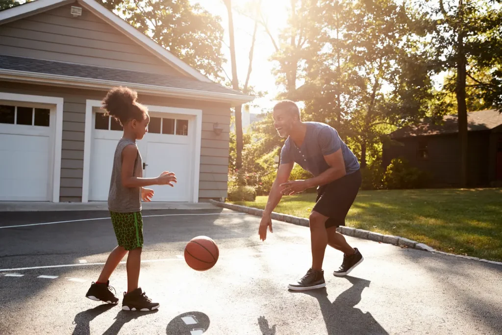 A man and a girl playing basketball in a driveway.