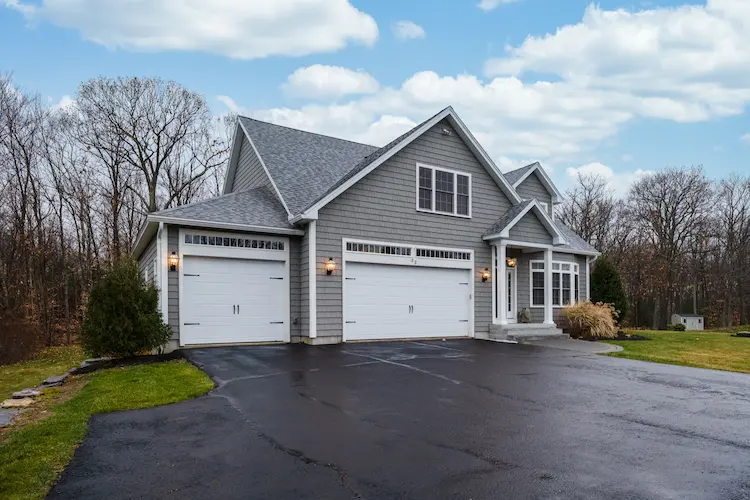 A home with two garages and a well-maintained driveway.|A man with a yellow shovel is clearing snow from a driveway