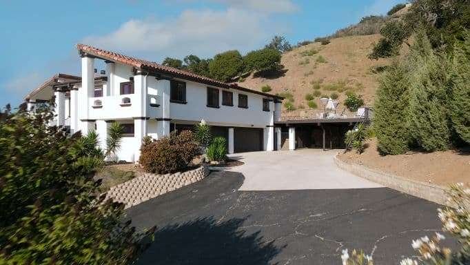 A residential home with a worn and cracked driveway in need of replacement. The house features beige siding and a green lawn, highlighting the need for a new, functional driveway installation.