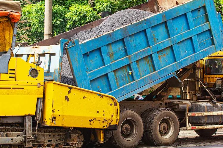 A dump truck is preparing for asphalt paving while driving down the street.