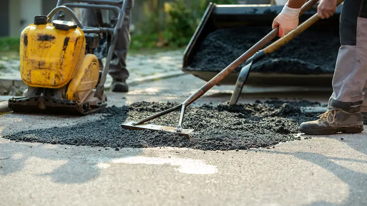 A man is working on an Asphalt Pavement Repair with a shovel.