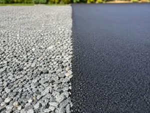 Close-up view highlighting the contrast in a gravel vs asphalt driveway, with a clear divide between the gravel surface on the left and freshly paved asphalt on the right.
